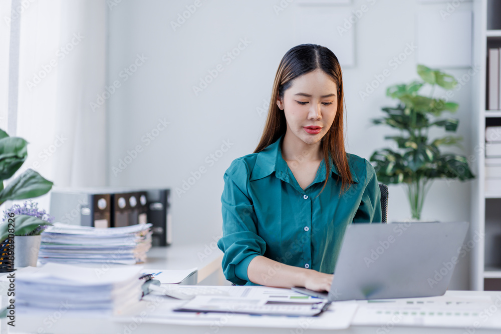 Asian woman in the workplace Work Hard writing notes on a pad from her laptop computer with analytical charts and graphs in front of her, business people concept Asian woman in the workplace Work Hard writing notes on a pad from her laptop computer with analytical charts and graphs in front of her, business people concept