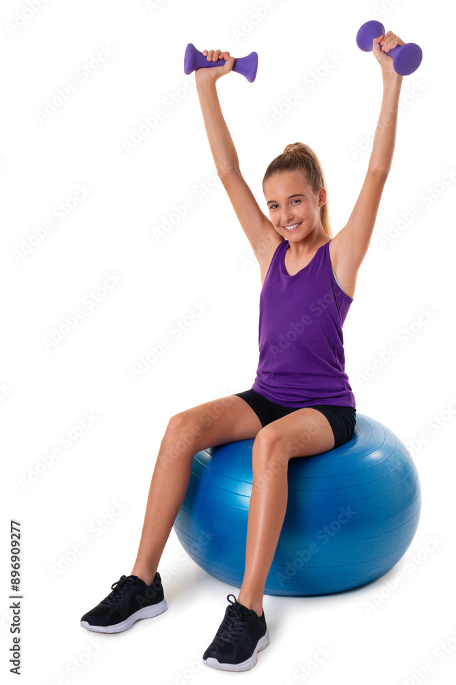 Slim and fit teen girl sitting a swiss blue ball and holding dumbbells with arms up. Isolated Slim and fit teen girl sitting a swiss blue ball and holding dumbbells with arms up. Isolated