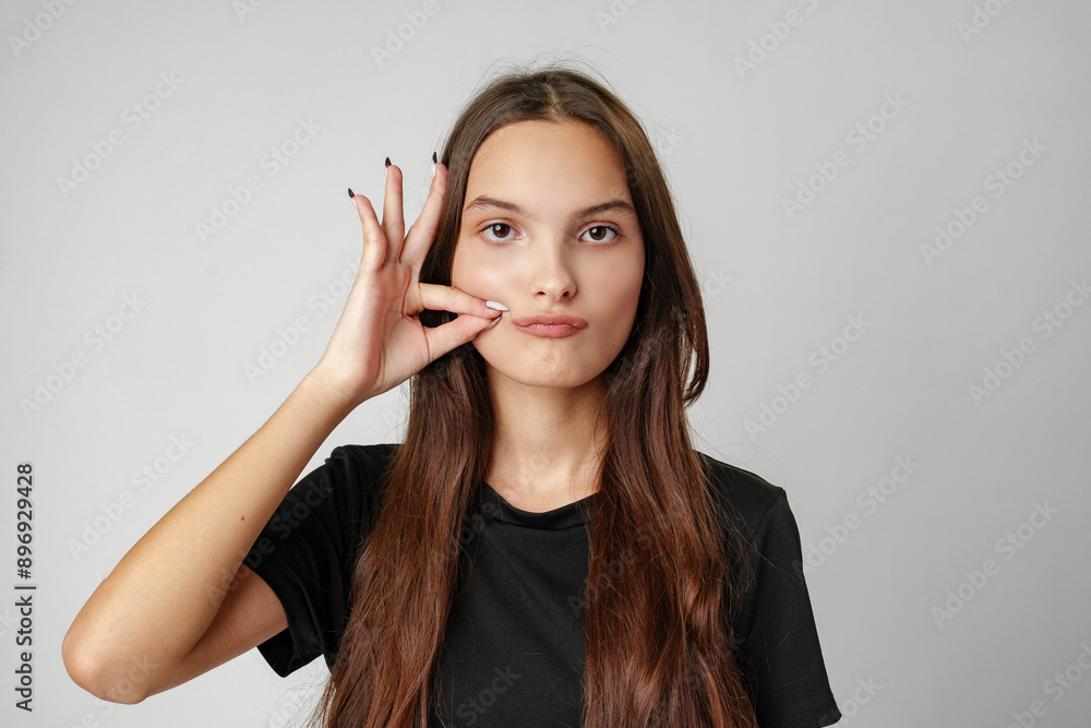 Young Woman With Long Brown Hair Makes a Gesture With Her Hand While Looking at the Camera Young Woman With Long Brown Hair Makes a Gesture With Her Hand While Looking at the Camera
