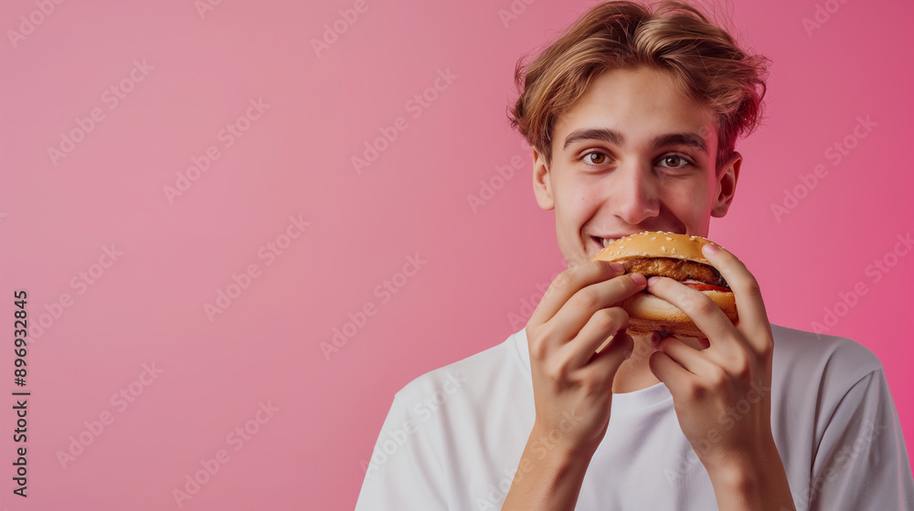 Young Man Enjoying a Delicious Hamburger in Front of a Pink Background Young Man Enjoying a Delicious Hamburger in Front of a Pink Background