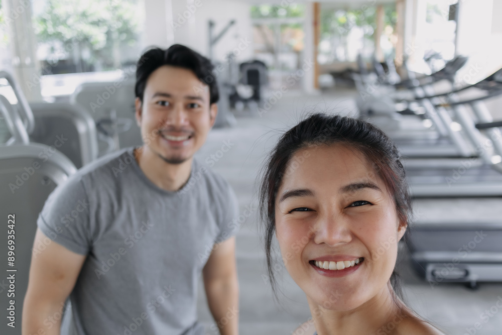 Fototapeta premium Happy asian Thai couples taking selfie while doing exercise at gym, happy workout together.