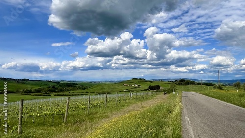 Landscape of a green field with a sky full of clouds, a small road, Tuscan hills.
