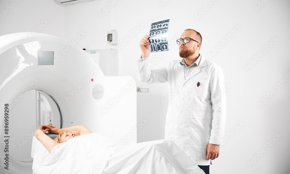 Obraz premium Medical computed tomography or MRI scanner. Doctor holding and examining results of MRI. Woman patient lying on CT scan bed. Concept of medicine, healthcare and modern diagnostics.