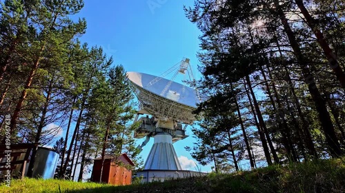 Exterior view of the Irbene radio telescope standing tall amidst deep woodland, highlighting its massive structure and technological significance photo