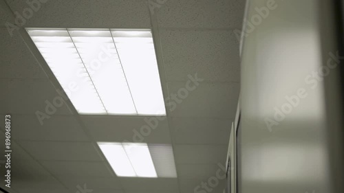 Fluorescent lights flicker on in a dim, textured ceiling office space