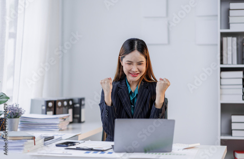 Charming Young happy asian business woman sitting on laptop computer in the office, asian employee business making report calculating balance Internal Revenue Service checking document.