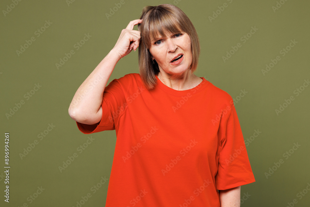 Elderly minded frustrated sad blonde woman 50s years old wear orange t-shirt casual clothes look camera scratch hold head isolated on plain pastel green background studio portrait. Lifestyle concept. Elderly minded frustrated sad blonde woman 50s years old wear orange t-shirt casual clothes look camera scratch hold head isolated on plain pastel green background studio portrait. Lifestyle concept.