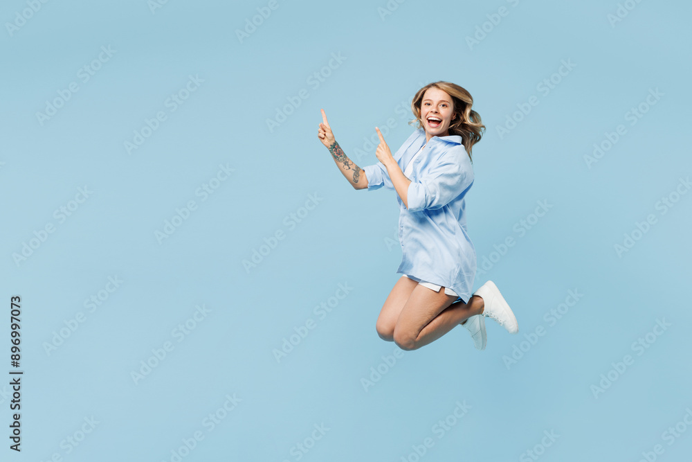 Full body young smiling happy woman she wears white top shirt casual clothes jump high point hand on advert area isolated on plain pastel light blue cyan background studio portrait. Lifestyle concept
