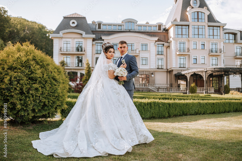 A bride and groom are standing in front of a large house, with the bride wearing a white dress and the groom wearing a blue suit A bride and groom are standing in front of a large house, with the bride wearing a white dress and the groom wearing a blue suit