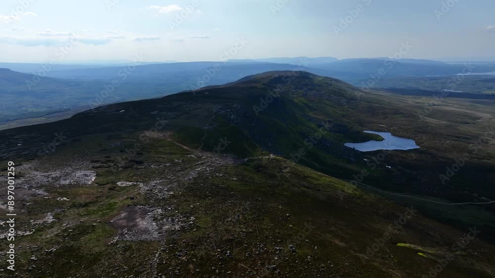 Cuilcagh Lakelands Geopark, County Fermanagh, Northern Ireland, June 2023. Drone pulls over the rocky mountain surface as shadows cover the natural landscape with Lough Atona in the distance. Cuilcagh Lakelands Geopark, County Fermanagh, Northern Ireland, June 2023. Drone pulls over the rocky mountain surface as shadows cover the natural landscape with Lough Atona in the distance.