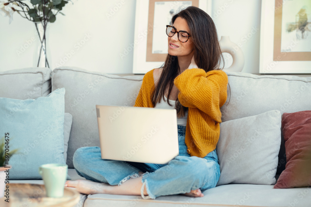 Tired young woman with neck pain using her laptop sitting on couch at home Tired young woman with neck pain using her laptop sitting on couch at home