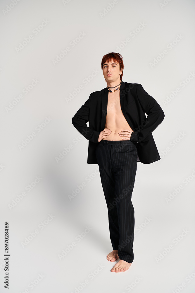 A stylish young man in a suit confidently stands with his hands on his hips in a studio with a grey background. A stylish young man in a suit confidently stands with his hands on his hips in a studio with a grey background.