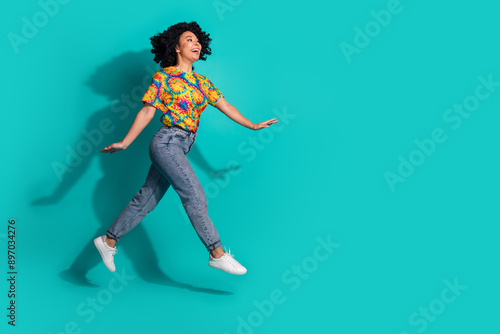 Full length photo of cheerful pretty lady dressed vintage t-shirt walking jumping high empty space isolated blue color background © deagreez