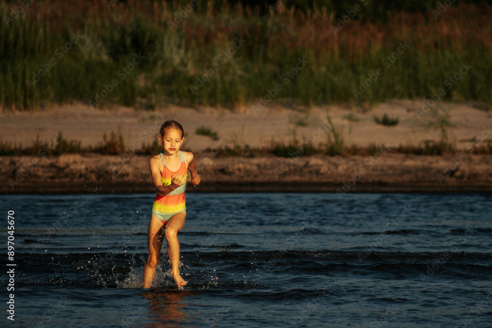 Fototapeta premium A girl in a colorful swimsuit playing energetically in the ocean waves, capturing a moment of joy and movement by the sea. The image emphasizes the fun and excitement of a summer day at the beach