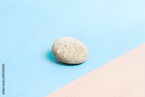 Single white stone on a pastel blue and pink background. Copy space