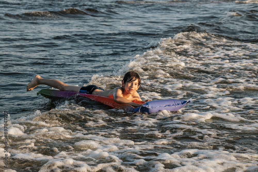 Fototapeta premium A boy riding an inflatable raft in the waves at the beach, capturing a moment of fun and adventure in the water. The image shows his determination and enjoyment as he navigates the waves.