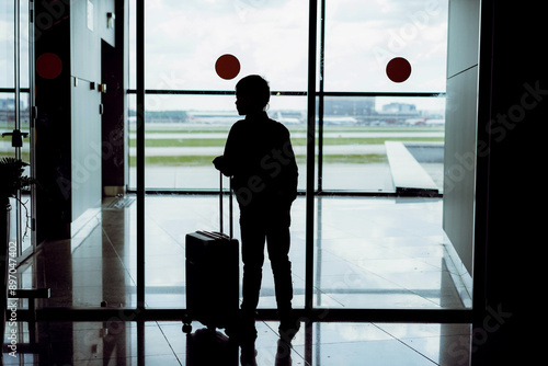 silhouette of caucasian boy with suitcase standing by the window in airport watching planes waiting for flight. Travelling concept