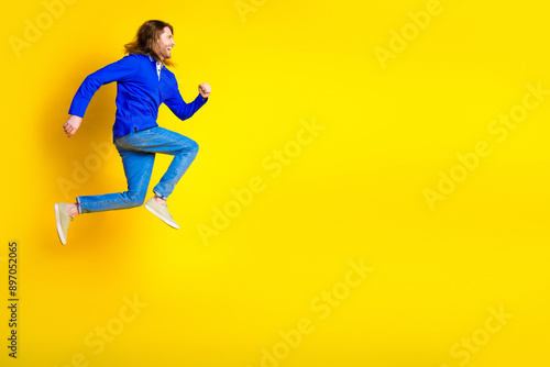 Photo of cheerful optimistic man wear trendy blue clothes jump up empty space isolated on yellow color background