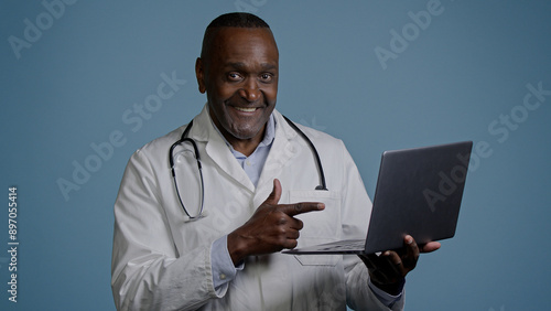 African american man doctor therapist ethnic male surgeon in white coat in blue background studio working on laptop consulting patient online remote diagnostics take useful information from internet