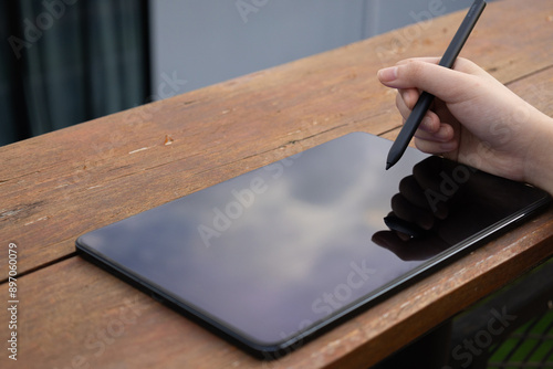 Hands of a business woman holding and using stylus pen for tablet pc on wooden table with blank screen for display your graphic. photo