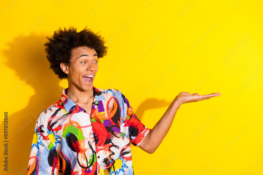 Photo of nice young man hold empty space wear shirt isolated on bright yellow color background Photo of nice young man hold empty space wear shirt isolated on bright yellow color background