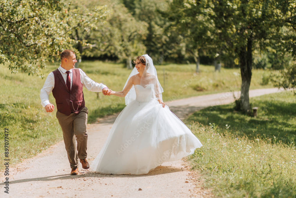 A bride and groom are walking down a dirt road. The bride is wearing a white dress and the groom is wearing a red vest A bride and groom are walking down a dirt road. The bride is wearing a white dress and the groom is wearing a red vest