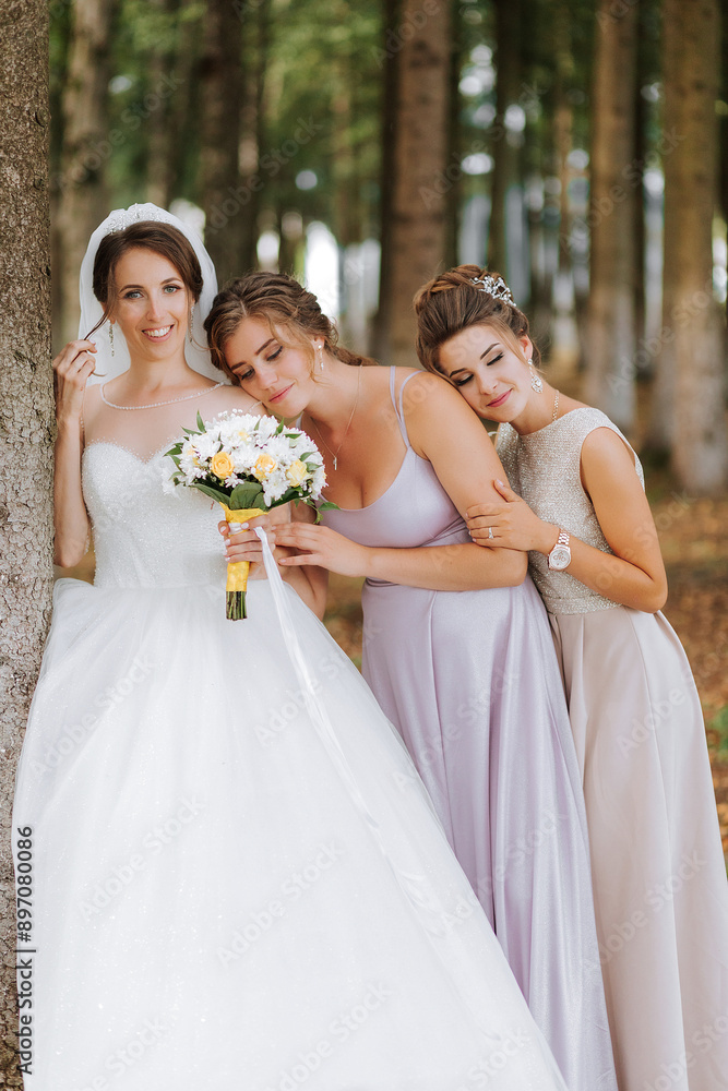 Three women are posing for a picture in a forest. One of them is wearing a wedding dress