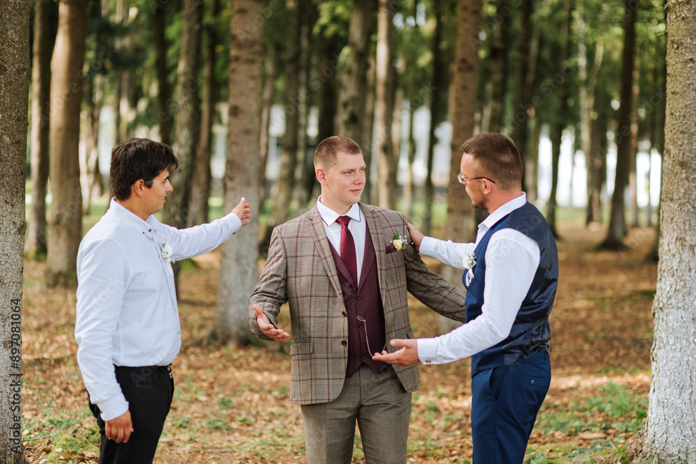 Three men are standing in a forest, one of them is wearing a suit and tie. They are all looking at something, possibly a camera or a piece of equipment. Scene is casual and relaxed Three men are standing in a forest, one of them is wearing a suit and tie. They are all looking at something, possibly a camera or a piece of equipment. Scene is casual and relaxed