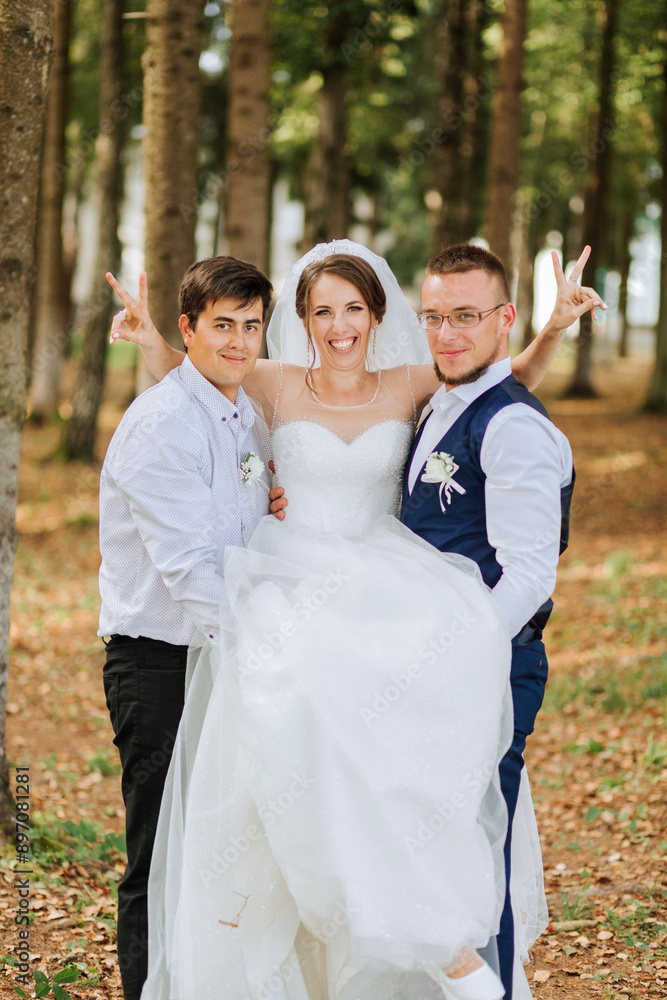 A bride and groom are posing for a picture with a man holding up the bride. The man is wearing a blue vest and glasses A bride and groom are posing for a picture with a man holding up the bride. The man is wearing a blue vest and glasses