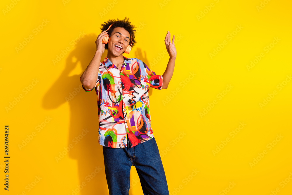 Photo of nice funky young man touch headphones wear shirt isolated on bright yellow color background Photo of nice funky young man touch headphones wear shirt isolated on bright yellow color background