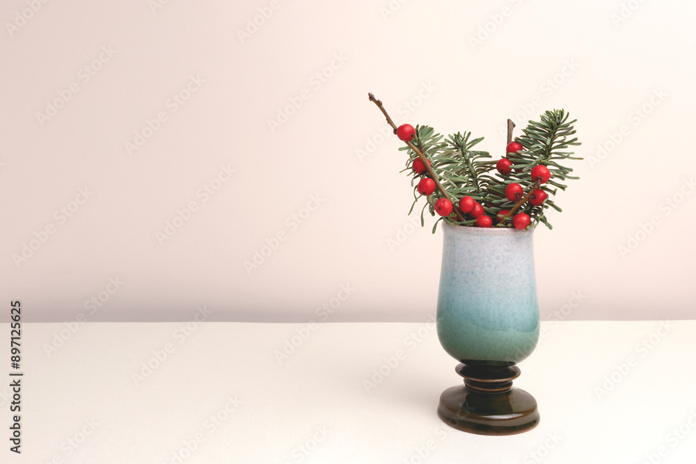 Fototapeta premium Nobilis fir and winterberry branches in a vase in front of beige background. Place for text.