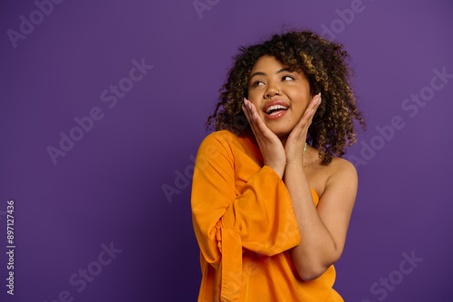 A beautiful African American woman wearing an orange shirt poses stylishly against a vibrant backdrop.