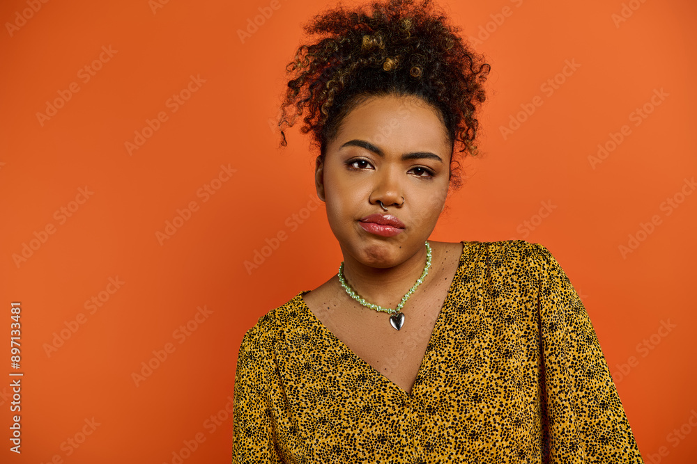 Stunning African American woman wearing a necklace poses against a vibrant orange backdrop. Stunning African American woman wearing a necklace poses against a vibrant orange backdrop.