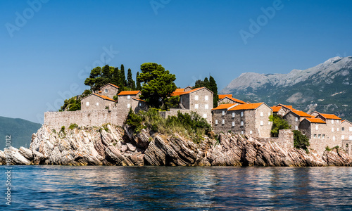 Scenic town on rocks in Montenegro, view from Adriatic sea on houses with orange roofs. Beautiful Mediterranean architecture with mountains on background