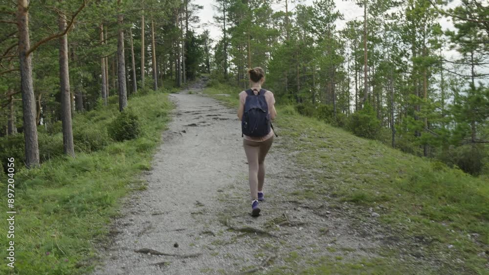 A female tourist with a backpack is trekking in the forest in summer. The concept of hiking and active life in nature. Slow motion A female tourist with a backpack is trekking in the forest in summer. The concept of hiking and active life in nature. Slow motion