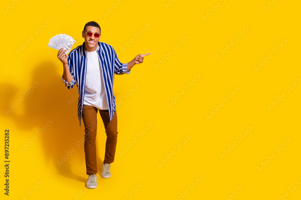 Full size photo of successful man dressed striped shirt in sunglass hold money directing empty space isolated on vivid color background Full size photo of successful man dressed striped shirt in sunglass hold money directing empty space isolated on vivid color background