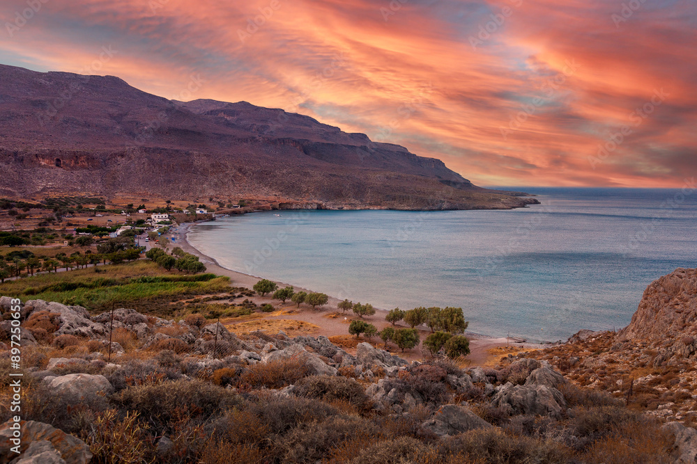 Stunning sunset over Kato Zakros Beach in Crete, Greece, highlighting the serene coastal village, rocky landscape, and calm waters under a vibrant sky