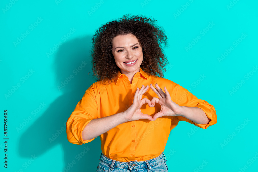 Photo of grateful friendly woman with wavy hairstyle dressed orange t-shirt showing heart symbol isolated on turquoise color background Photo of grateful friendly woman with wavy hairstyle dressed orange t-shirt showing heart symbol isolated on turquoise color background