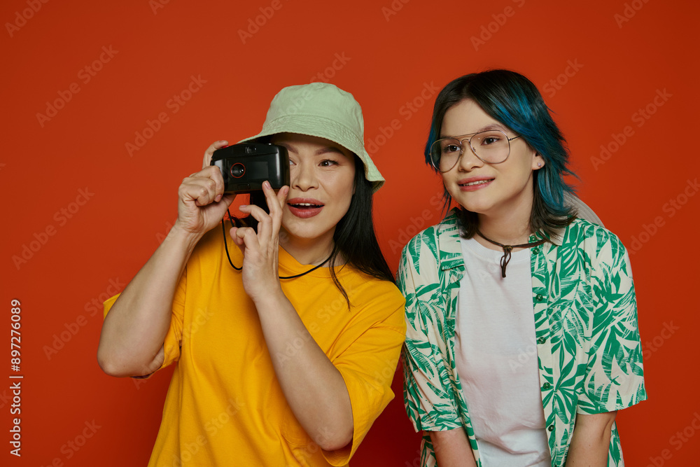 An Asian mother and her teenage daughter stand together in a studio, showcasing unity and familial bond on an orange background. An Asian mother and her teenage daughter stand together in a studio, showcasing unity and familial bond on an orange background.