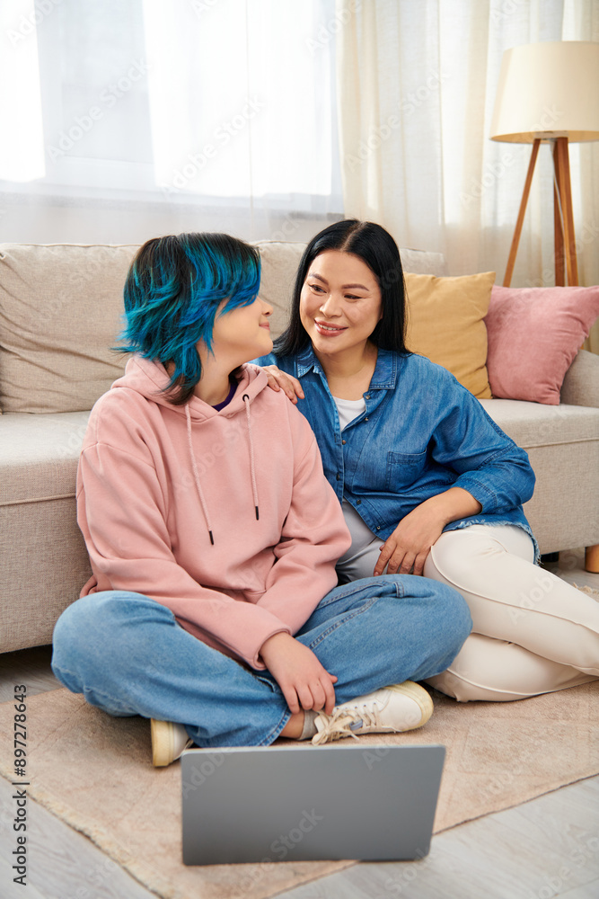 An Asian mother and her teenage daughter sit on the floor, engrossed in a laptop screen, spending quality time together at home. An Asian mother and her teenage daughter sit on the floor, engrossed in a laptop screen, spending quality time together at home.