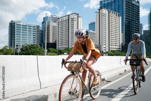 A young couple riding their bikes over a bridge in the city.