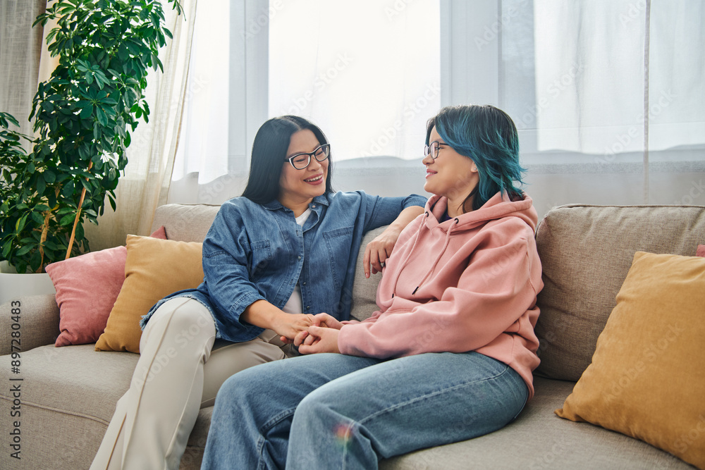 An Asian mother and her teenage daughter in casual wear having a heartfelt conversation while sitting on a cozy couch. An Asian mother and her teenage daughter in casual wear having a heartfelt conversation while sitting on a cozy couch.