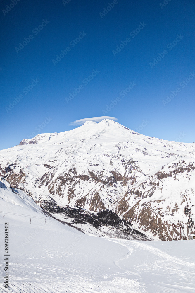Obraz premium Snowy mountain peaks of Elbrus and nearby peaks in winter on a sunny day