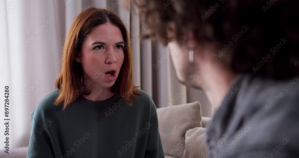 Over the shoulder an angry brunette girl in a green shirt swears with her boyfriend while talking about relationships and life at home in a modern apartment on the sofa Over the shoulder an angry brunette girl in a green shirt swears with her boyfriend while talking about relationships and life at home in a modern apartment on the sofa