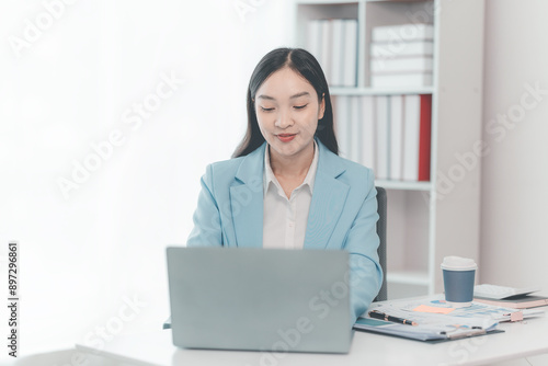 Happy Asian businesswoman working with laptop, analyzing business documents with financial graphs, market reports on digital tablet. accounting concepts