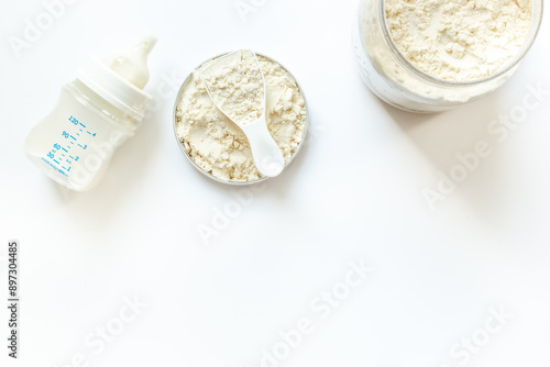 Jar of powdered milk for baby food with bottle of milk and spoon, top view