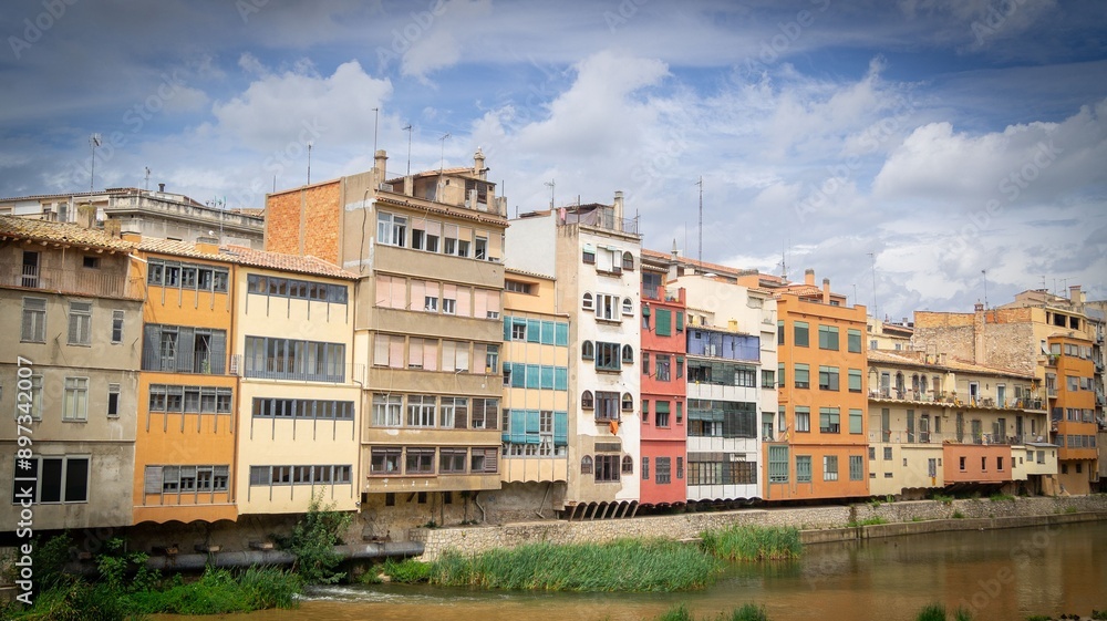 Colorful buildings along the Onyar River in Girona, Spain under a cloudy sky Colorful buildings along the Onyar River in Girona, Spain under a cloudy sky
