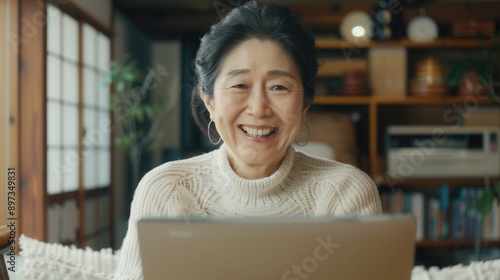 Thrilled Japanese woman with a beaming smile and laptop in a cozy home setting reflecting her success