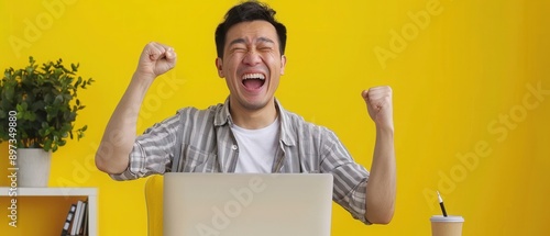 Elated Japanese man pumping his fist in the air with a laptop open in a creative studio environment