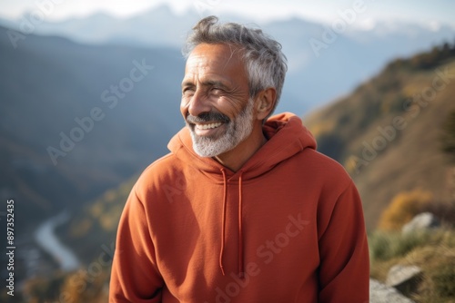 Portrait of a joyful indian man in his 60s dressed in a comfy fleece pullover over backdrop of mountain peaks